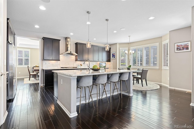 6728 S Catawba Way, Aurora, CO 80016 - kitchen with wall chimney exhaust hood, a center island with sink, recessed lighting, a kitchen bar, and cooktop