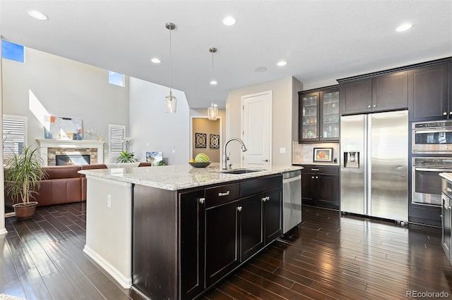 6728 S Catawba Way, Aurora, CO 80016 - kitchen featuring stainless steel appliances, dark wood-style flooring, glass insert cabinets, an island with sink, and a fireplace