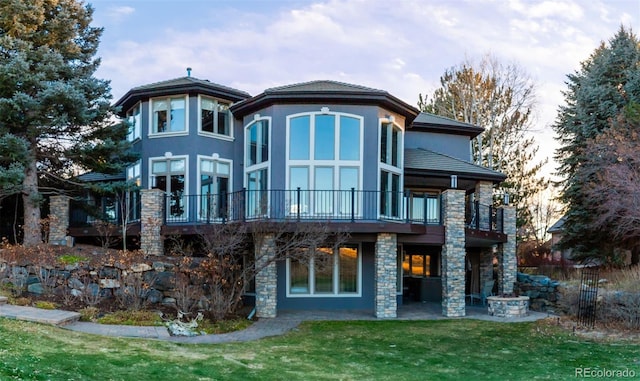 rear view of property with stone siding, a patio area, a yard, and stucco siding