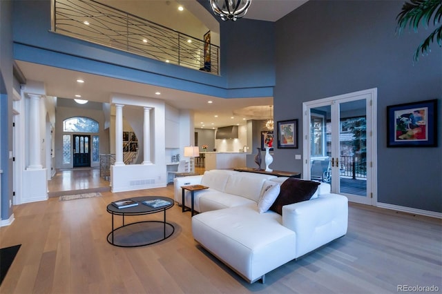 living room with french doors, ornate columns, an inviting chandelier, light hardwood / wood-style flooring, and a high ceiling