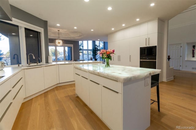 kitchen with a kitchen island, black appliances, sink, kitchen peninsula, and light wood-type flooring