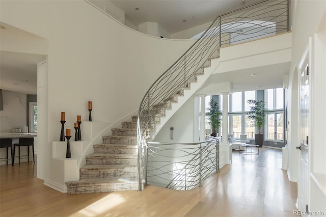 stairs with hardwood / wood-style flooring, ornate columns, and a towering ceiling