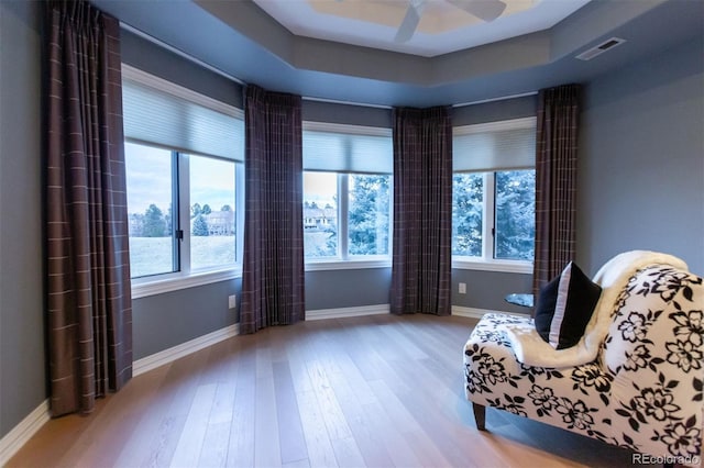 sitting room featuring ceiling fan, light wood-type flooring, and a tray ceiling