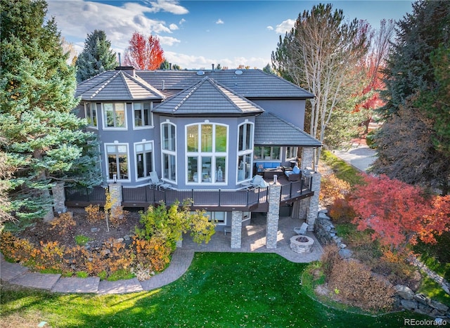 rear view of property featuring a lawn, an outdoor living space with a fire pit, a patio, and a deck