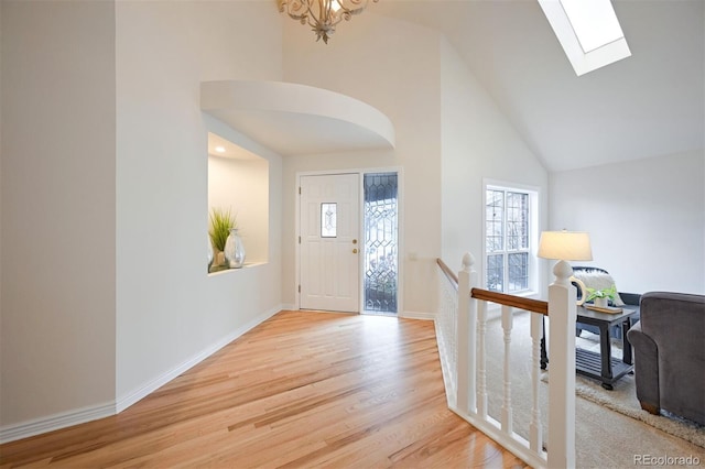 entrance foyer with a skylight, high vaulted ceiling, and light hardwood / wood-style flooring