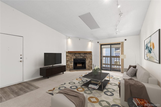 living room featuring rail lighting, a skylight, a textured ceiling, a stone fireplace, and light colored carpet