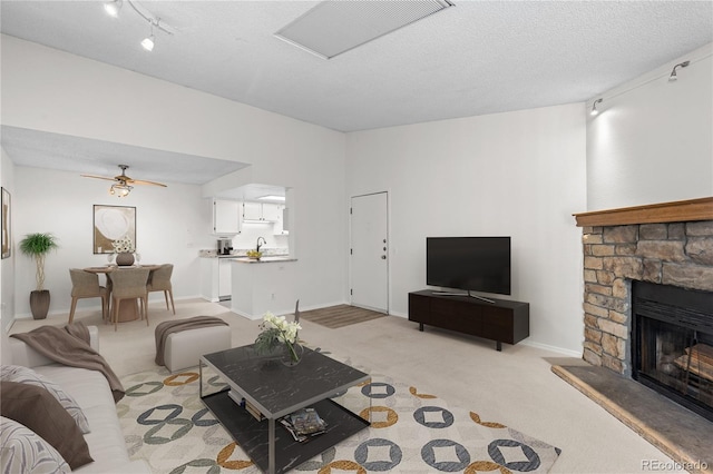 carpeted living room with ceiling fan, rail lighting, a stone fireplace, and a textured ceiling