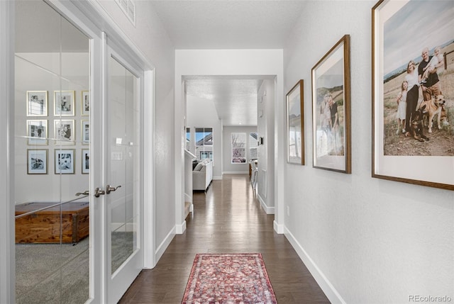 hallway with dark wood finished floors, a textured ceiling, and baseboards