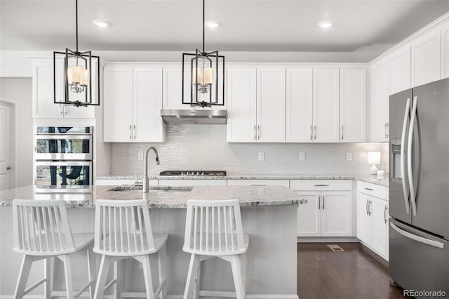kitchen featuring white cabinets, a sink, dark wood-style flooring, under cabinet range hood, and appliances with stainless steel finishes