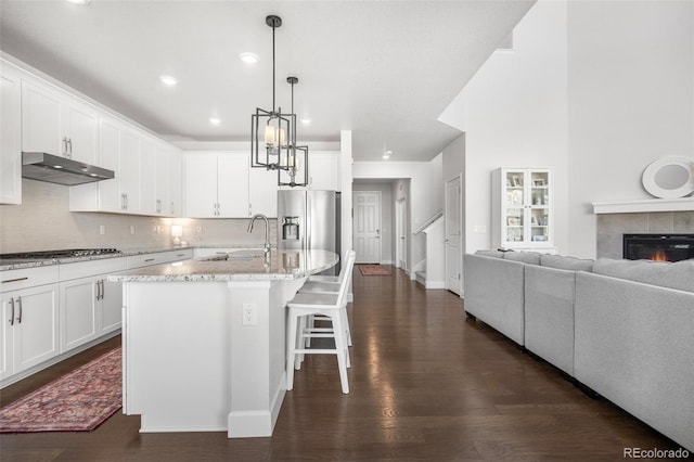 kitchen featuring under cabinet range hood, stainless steel fridge with ice dispenser, a sink, dark wood-type flooring, and gas cooktop