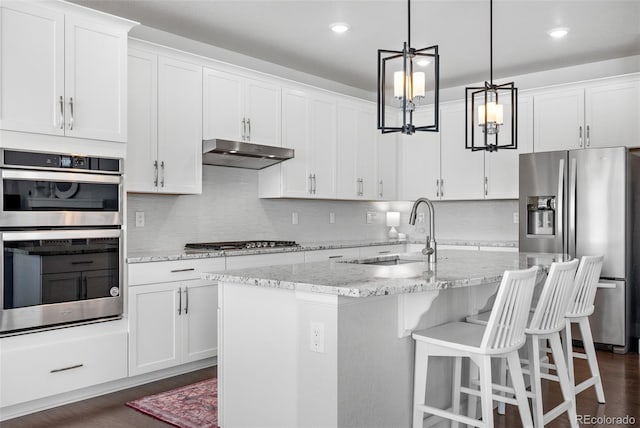 kitchen featuring stainless steel appliances, a sink, white cabinetry, under cabinet range hood, and dark wood-type flooring
