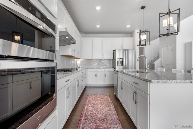 kitchen with under cabinet range hood, backsplash, a sink, a chandelier, and appliances with stainless steel finishes