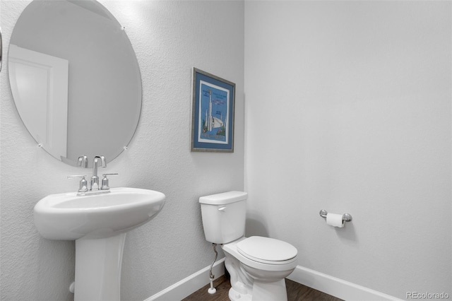 half bathroom with wood finished floors, toilet, baseboards, and a sink