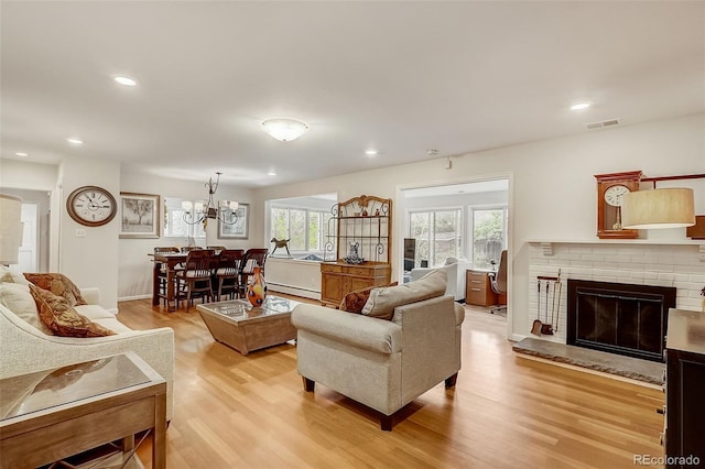 living room with light hardwood / wood-style floors, a chandelier, a fireplace, and baseboard heating