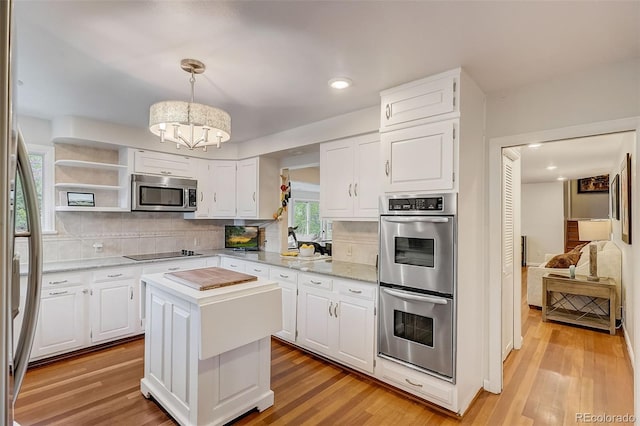 kitchen with light wood-type flooring, white cabinetry, backsplash, appliances with stainless steel finishes, and a kitchen island