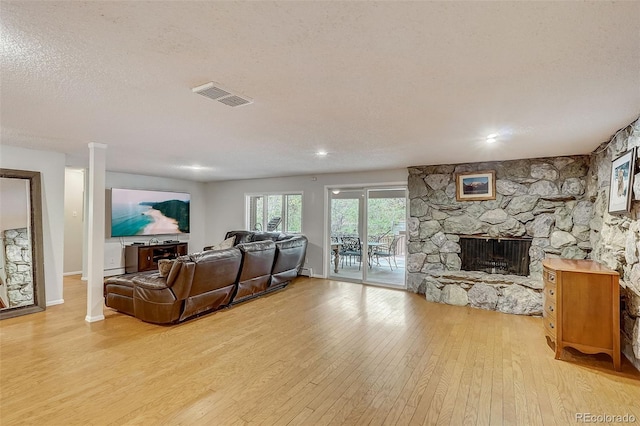 living room with light hardwood / wood-style flooring, a baseboard radiator, a textured ceiling, and a stone fireplace