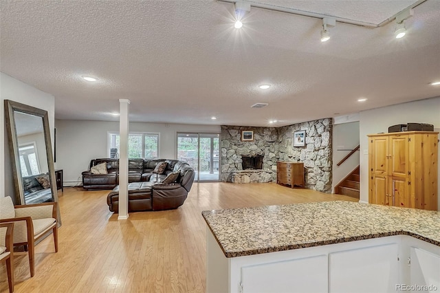 kitchen featuring white cabinets, a baseboard radiator, light hardwood / wood-style flooring, a stone fireplace, and a textured ceiling