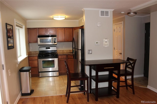 kitchen featuring crown molding, brown cabinetry, stainless steel appliances, baseboards, and visible vents