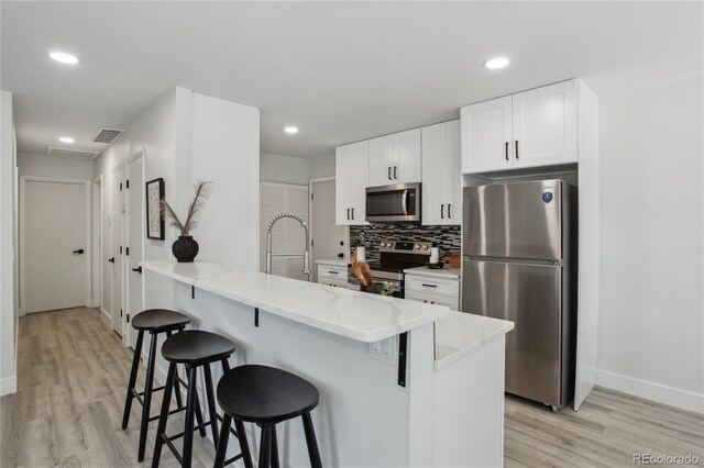 7970 Chase Cir Unit 85, Arvada, CO 80003 - kitchen featuring appliances with stainless steel finishes, light wood-type flooring, a kitchen bar, white cabinetry, and recessed lighting