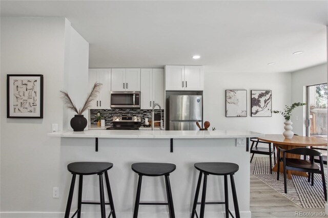 7970 Chase Cir Unit 85, Arvada, CO 80003 - kitchen featuring stainless steel appliances, a kitchen bar, a peninsula, backsplash, and light wood-style floors