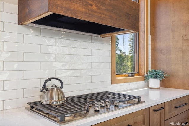 41 Barton Ridge Dr, Breckenridge, CO 80424 - kitchen featuring stainless steel gas cooktop, brown cabinets, exhaust hood, tasteful backsplash, and light stone countertops