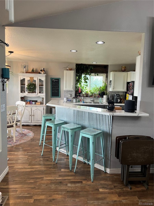 825 Cherokee St, Strasburg, CO 80136 - kitchen with white cabinetry, a breakfast bar area, dark wood-style floors, backsplash, and lofted ceiling
