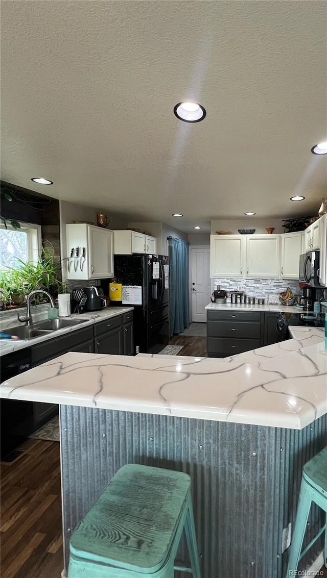 825 Cherokee St, Strasburg, CO 80136 - kitchen featuring light stone counters, a textured ceiling, white cabinets, decorative backsplash, and a breakfast bar area