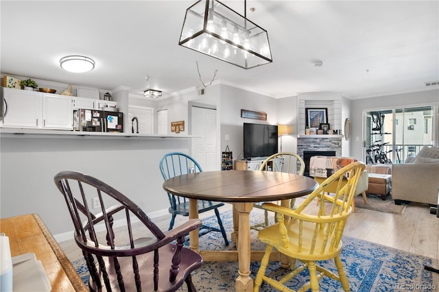 dining room featuring ornamental molding, light hardwood / wood-style flooring, and a fireplace