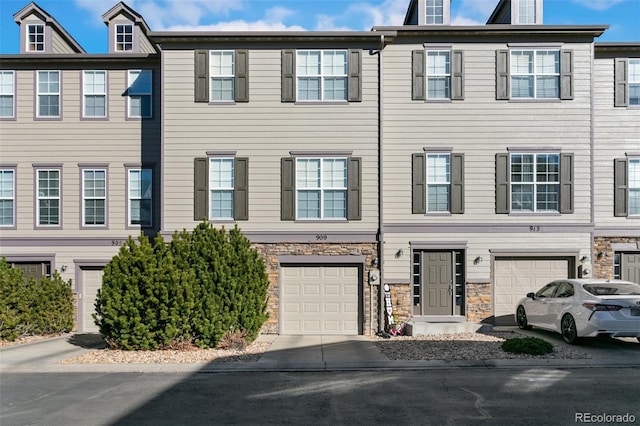 townhome / multi-family property with an attached garage, stone siding, and driveway