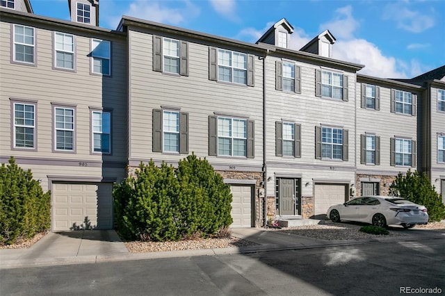 townhome / multi-family property featuring a garage, stone siding, and driveway