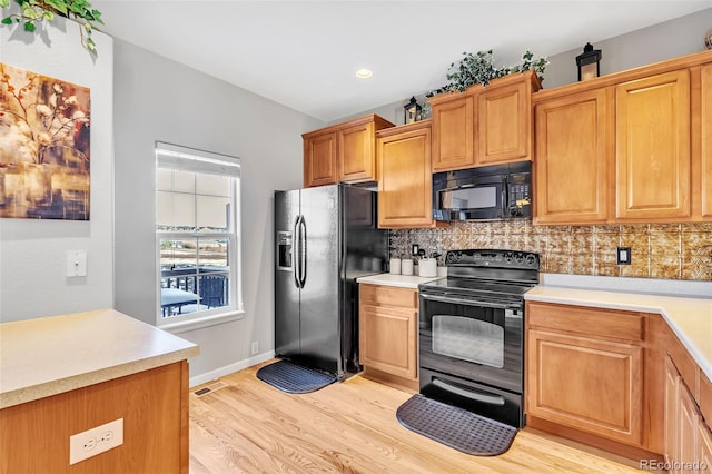 kitchen featuring black appliances, light wood-style flooring, light countertops, and backsplash