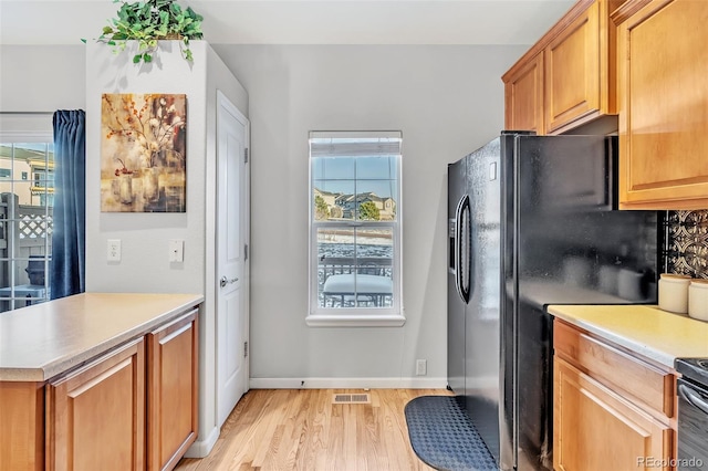 kitchen with light countertops, black refrigerator with ice dispenser, light wood-style flooring, and a healthy amount of sunlight