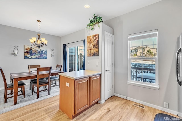 kitchen with a peninsula, brown cabinets, light wood-style flooring, and a notable chandelier