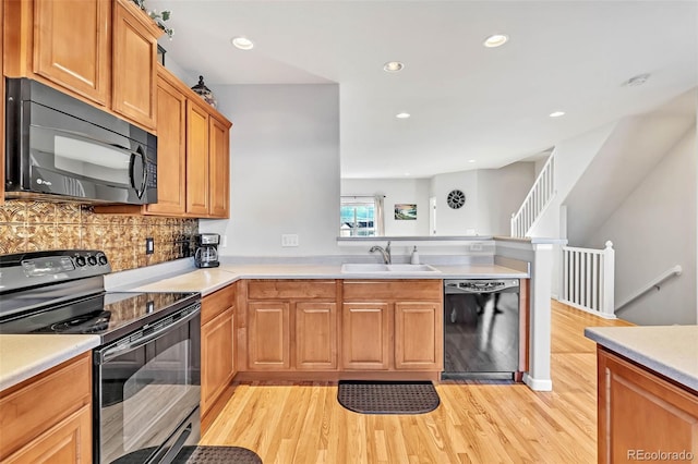 kitchen featuring a peninsula, a sink, light countertops, black appliances, and light wood finished floors