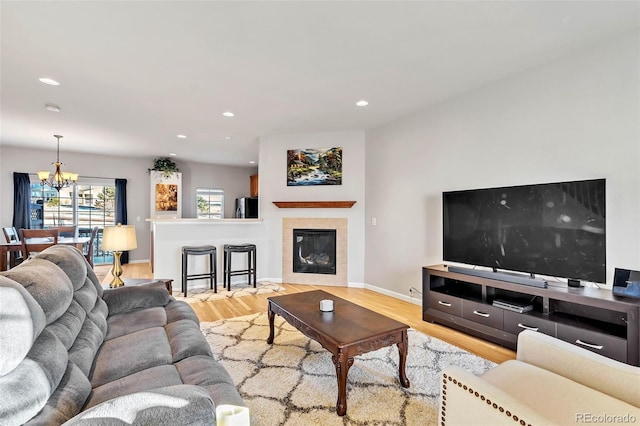 living area with light wood finished floors, baseboards, a tile fireplace, a notable chandelier, and recessed lighting