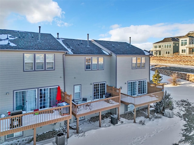 snow covered property featuring a shingled roof and a deck