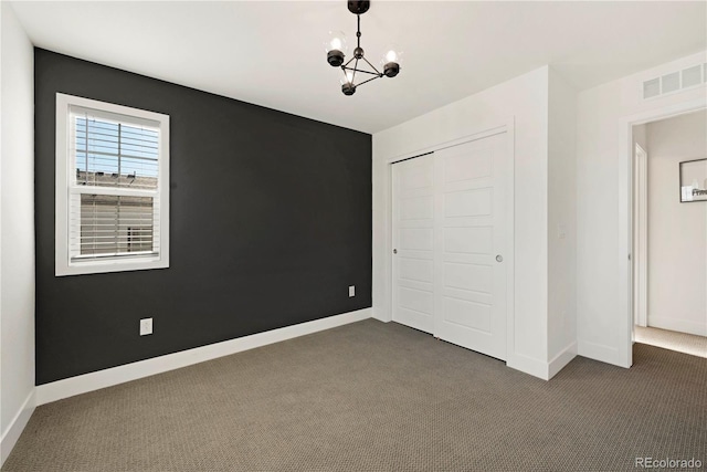 unfurnished bedroom featuring a notable chandelier, dark carpet, and a closet