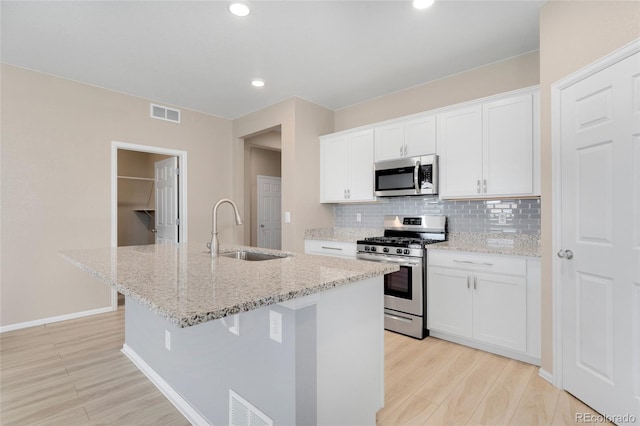 15525 Quince Cir, Thornton, CO 80602 - kitchen with appliances with stainless steel finishes, a sink, light wood-type flooring, an island with sink, and decorative backsplash