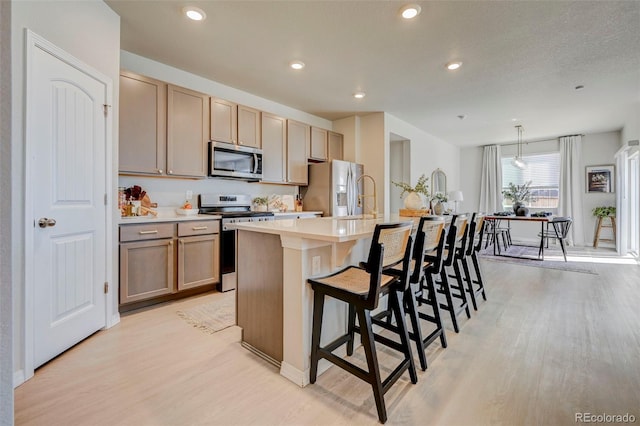 10499 Rolling Peaks Dr, Peyton, CO 80831 - kitchen featuring stainless steel appliances, a kitchen island with sink, light wood finished floors, a breakfast bar, and light countertops