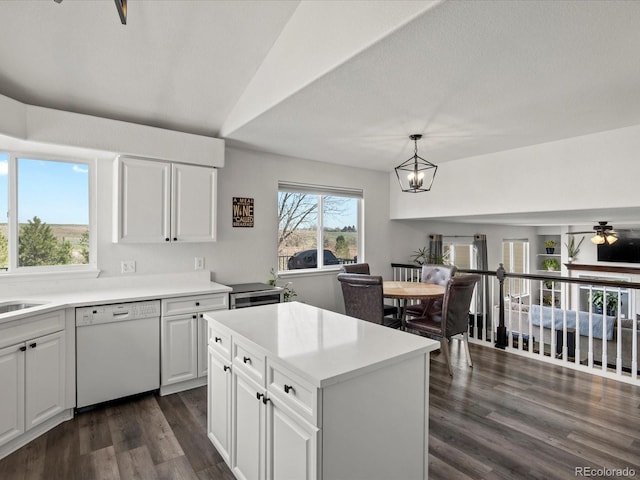kitchen with white dishwasher, white cabinets, a sink, dark wood finished floors, and a notable chandelier