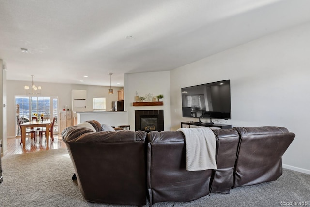 living room featuring carpet floors, a tiled fireplace, and a notable chandelier