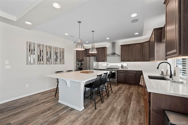 kitchen featuring appliances with stainless steel finishes, hanging light fixtures, a kitchen island, wall chimney exhaust hood, and sink