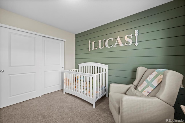 carpeted bedroom with a closet, wood walls, and a crib