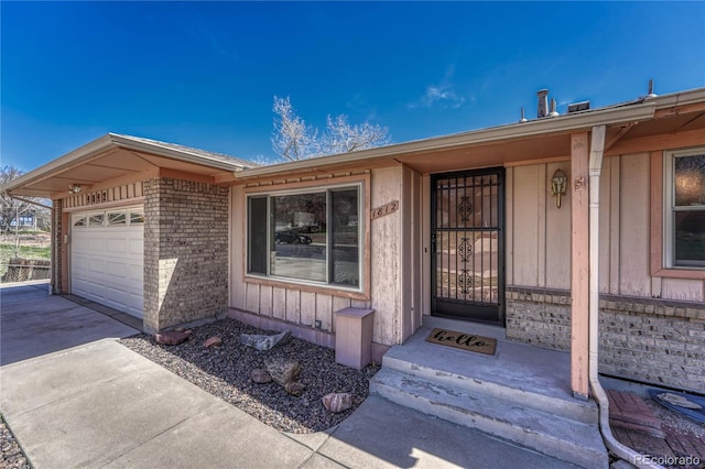 view of exterior entry featuring a garage, concrete driveway, and brick siding
