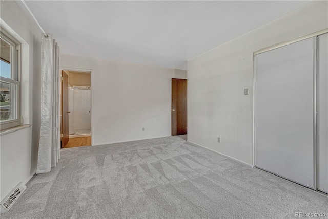 unfurnished bedroom featuring carpet flooring, visible vents, and ensuite bath