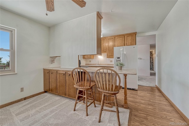 kitchen featuring baseboards, white fridge with ice dispenser, ceiling fan, a breakfast bar, and a peninsula