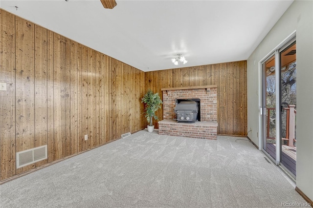 unfurnished living room featuring visible vents, a wood stove, carpet flooring, and wood walls