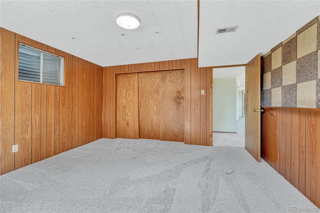 unfurnished room with wood walls, carpet flooring, and visible vents