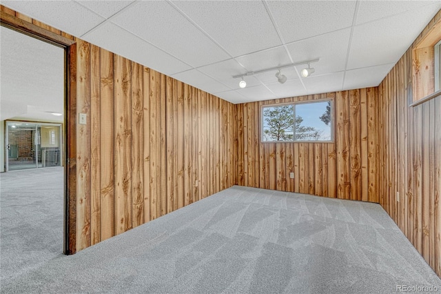 carpeted spare room with wood walls and track lighting