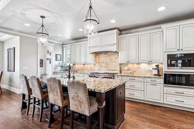 kitchen featuring decorative light fixtures, white cabinetry, crown molding, light stone countertops, and a center island with sink